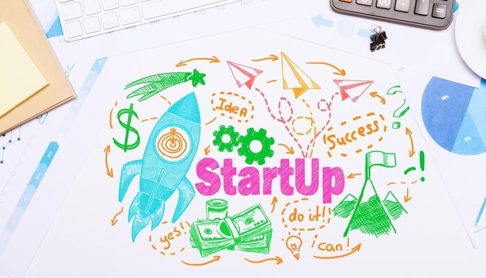 Colorful illustration symbolizing the startup journey with a rocket, dollar signs, gears, and arrows, highlighting the path to success. The word 'StartUp' is prominently featured, emphasizing the importance of a startup loan, with motivating phrases like 'Do it!' and 'Success'.