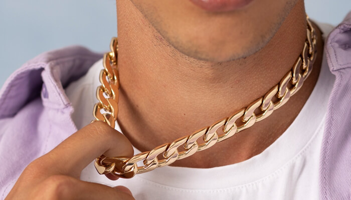 Close-up of a man wearing two gold Cuban link chains, one around his neck and the other held in his hand, showcasing a trendy and bold style.